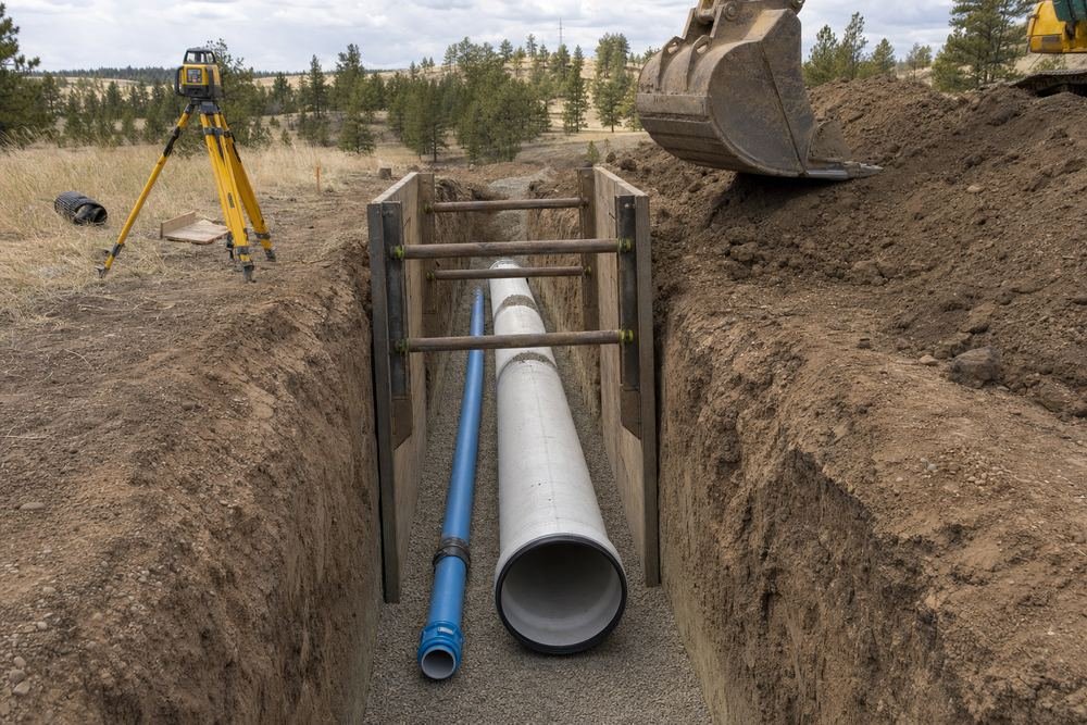 New sewer main and water line bedded in clean gravel inside a shored trench